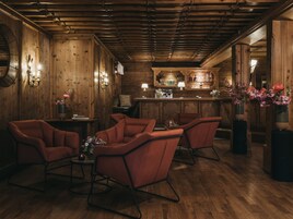 Una habitación acogedora con paredes de madera y una zona de bar. Hay cuatro sillas rojas y una mesa con flores.