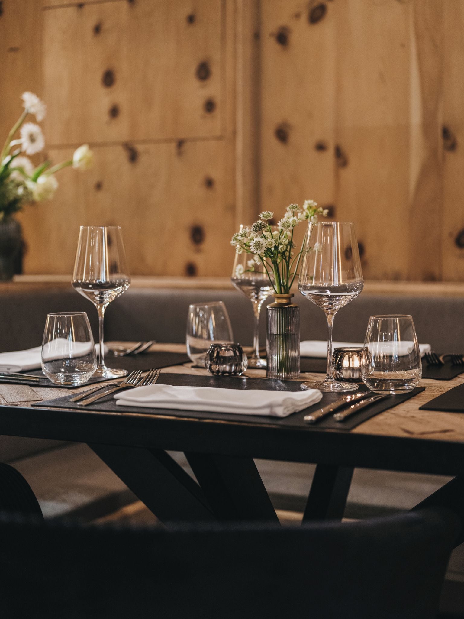 A restaurant table set with wine glasses, a vase with flowers, and cutlery.