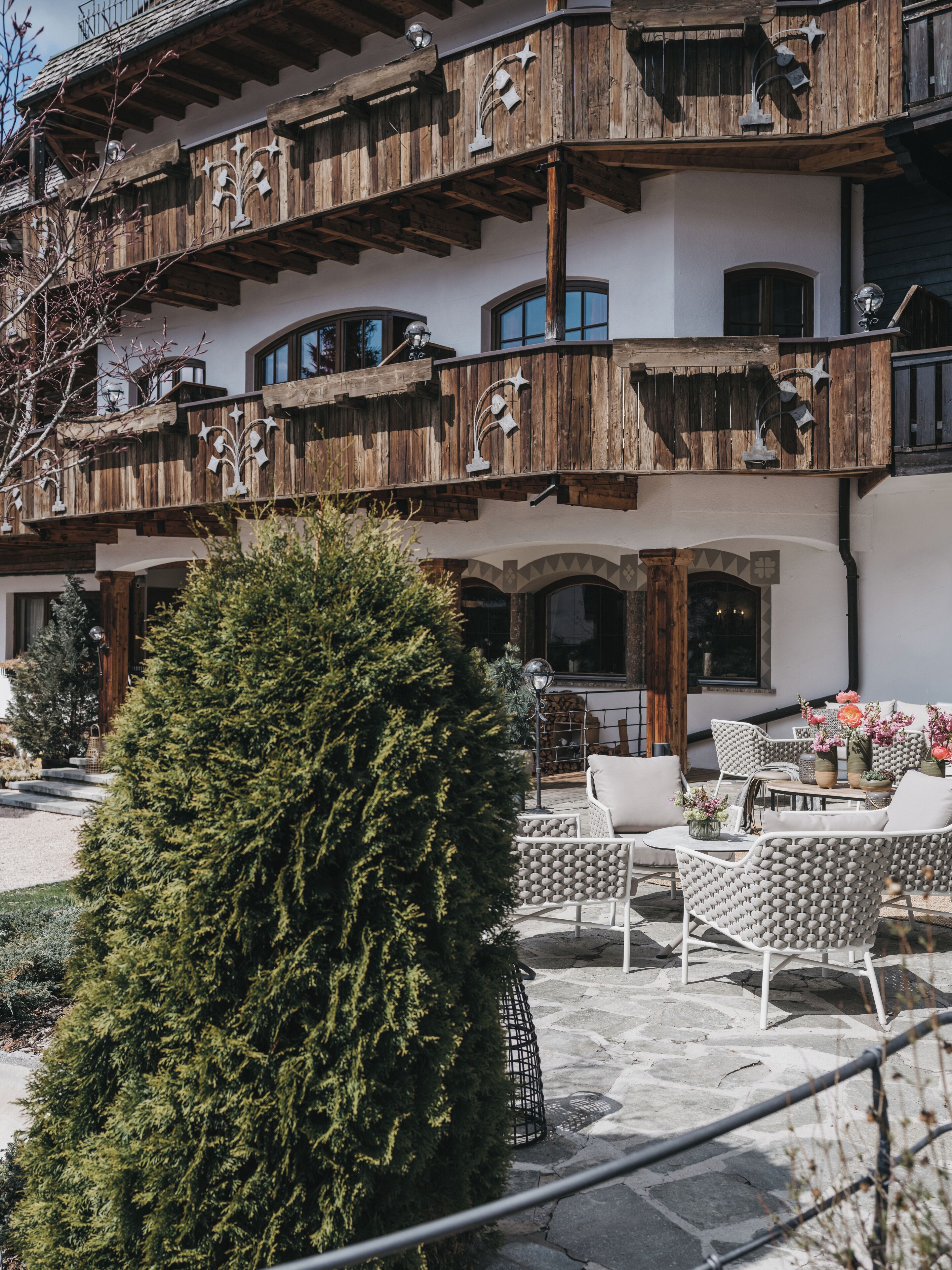 A multi-story building with wooden balconies, outdoor seating, and a large evergreen tree.