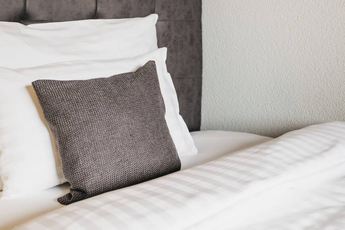 A neatly made bed with a tufted headboard, white bedding, and a textured pillow.