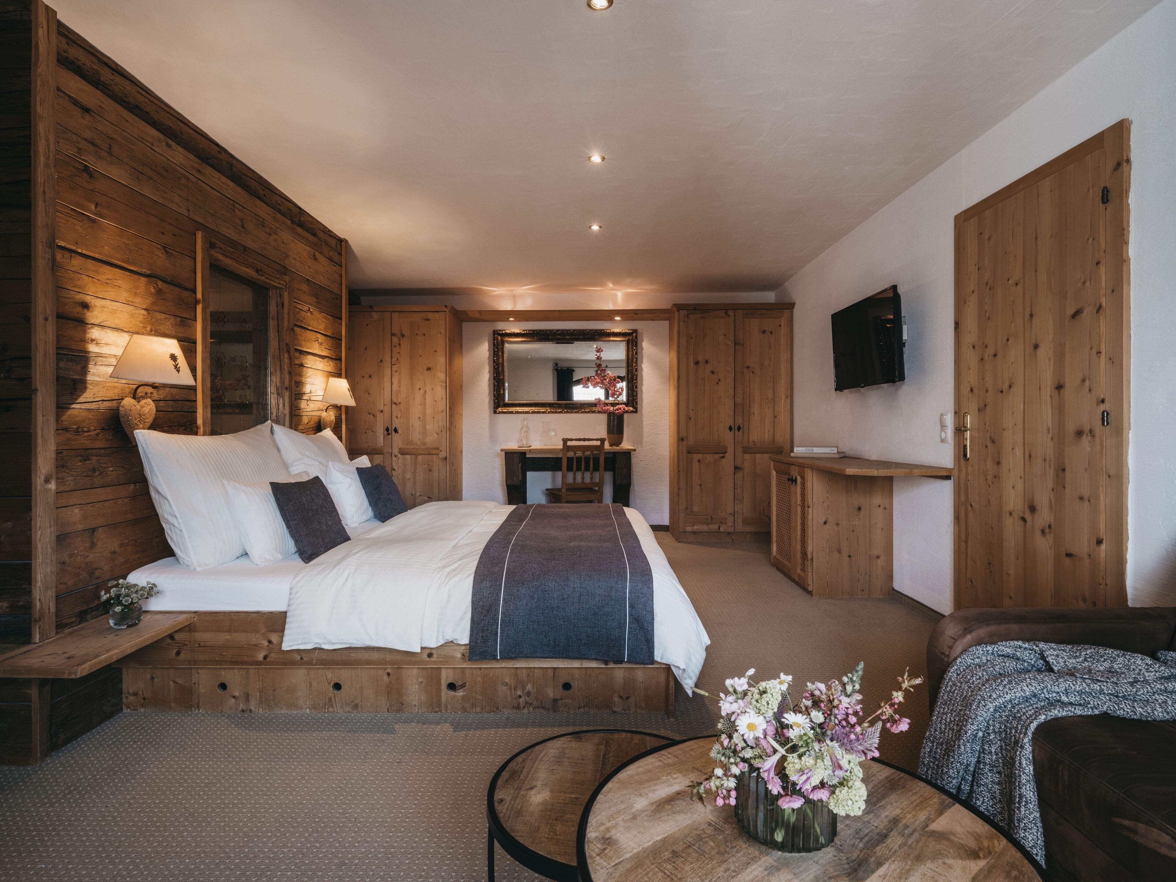 A wooden bedroom with a bed, bedside tables, a desk, and a TV.
