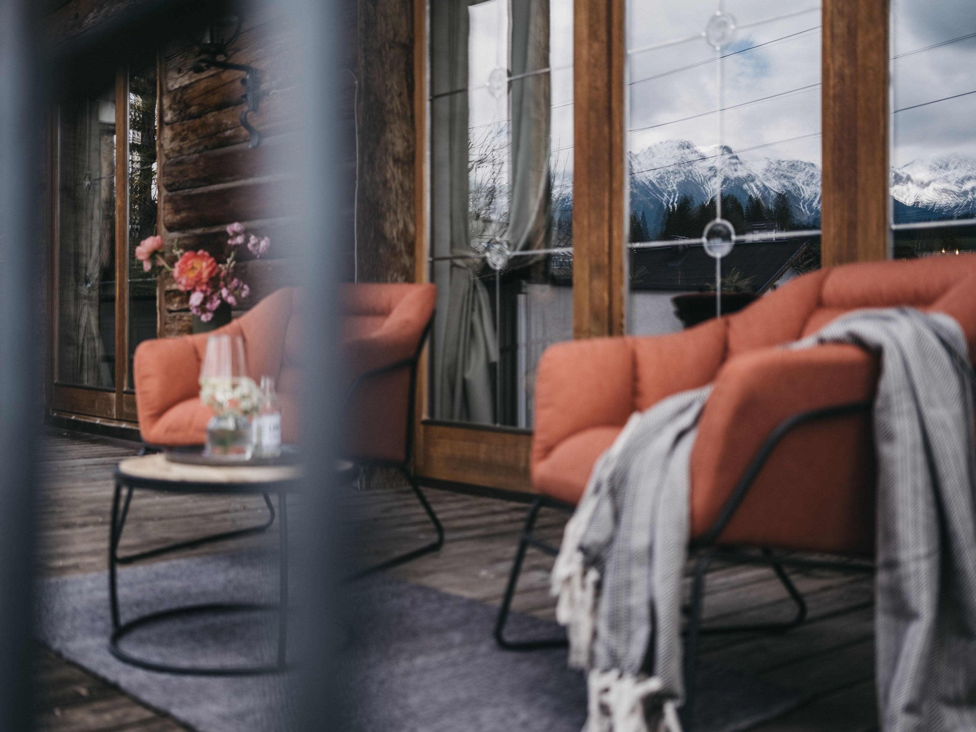 Una habitación con piso de madera, un sofá, una mesa con un vaso y vistas a montañas nevadas a través de amplios ventanales.