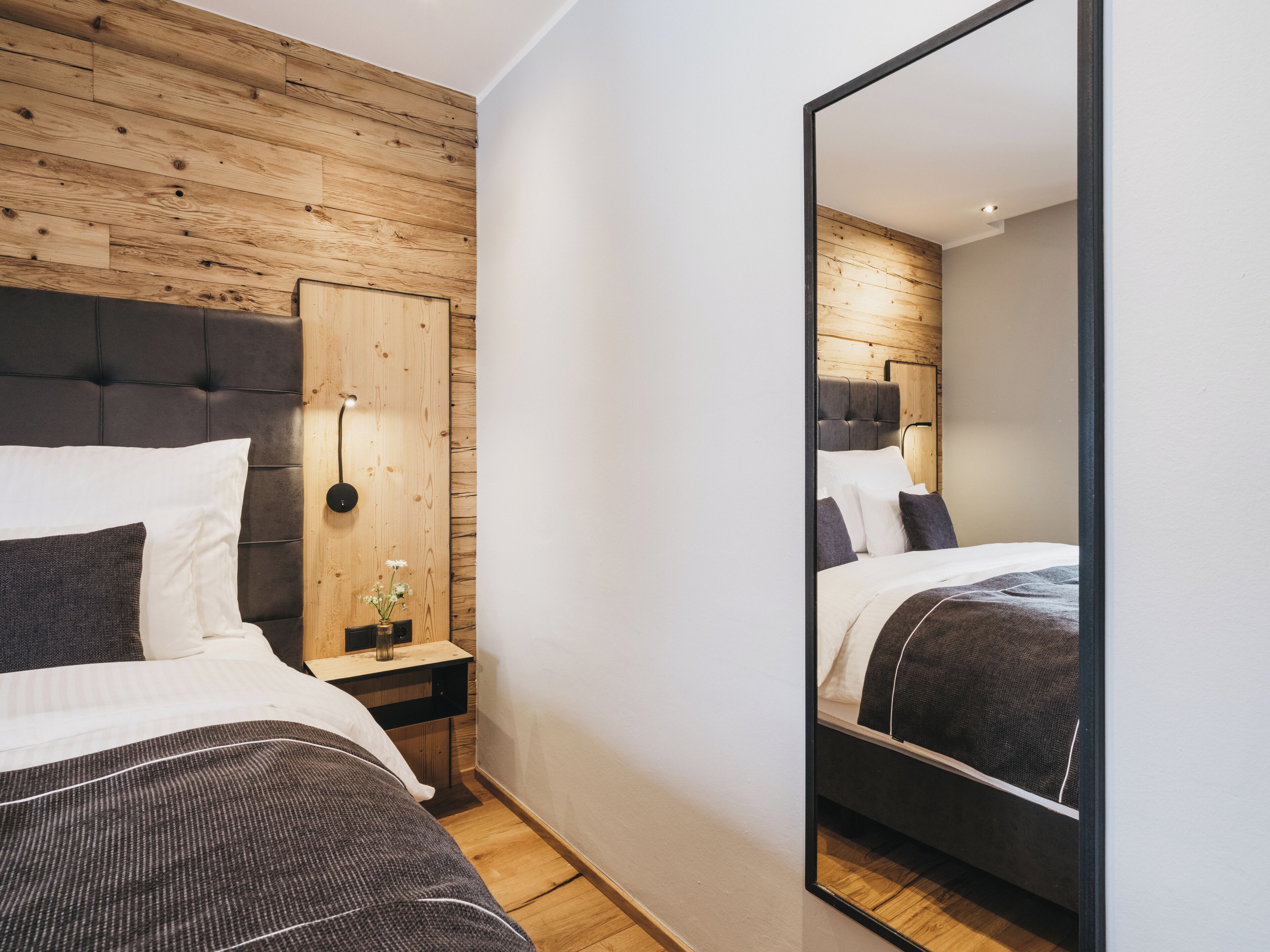 Un dormitorio moderno con cabecera de madera, una mesita de noche con un florero y un espejo grande.