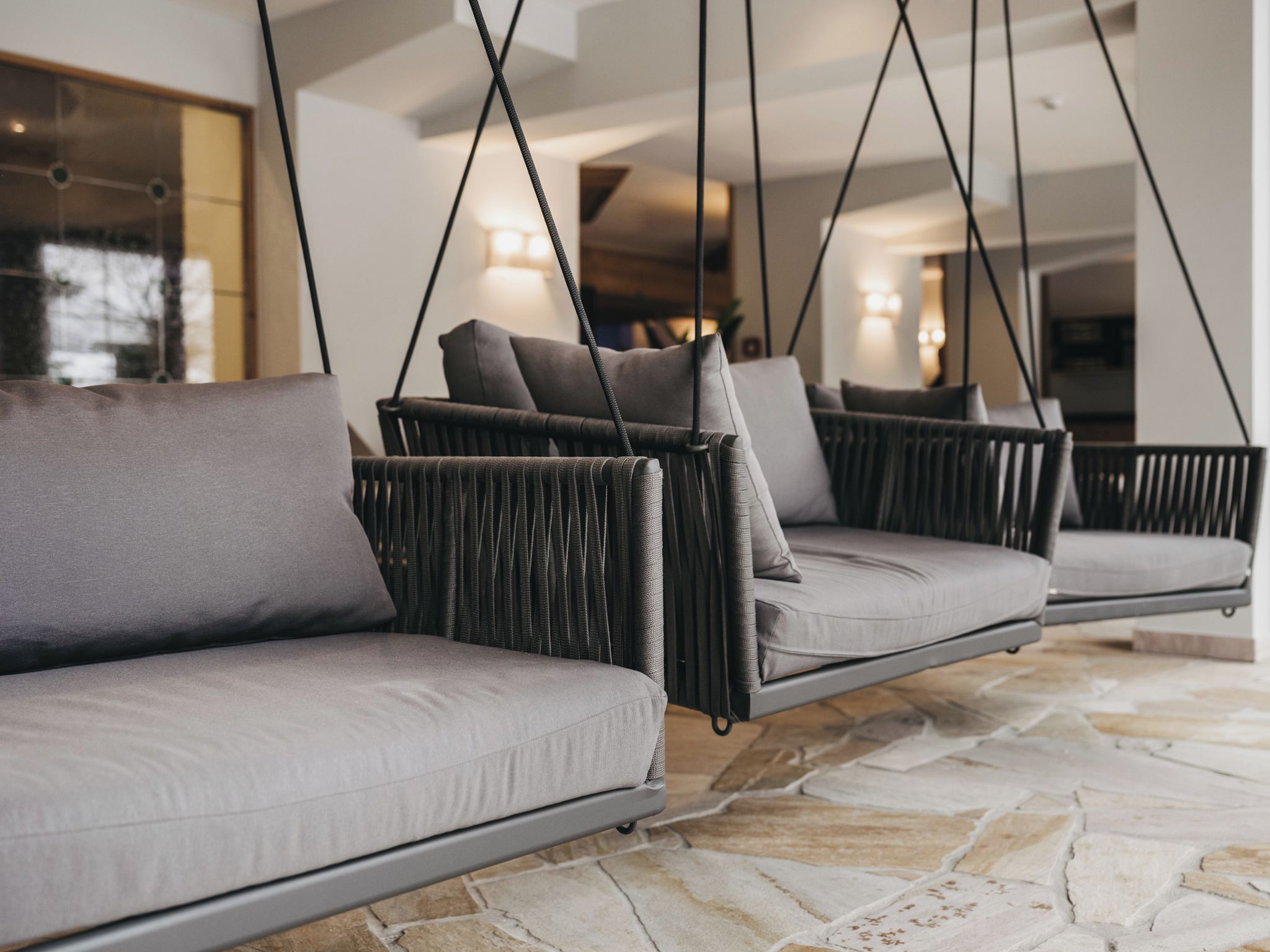 A modern interior with a stone floor and a suspended seating area with grey cushions.