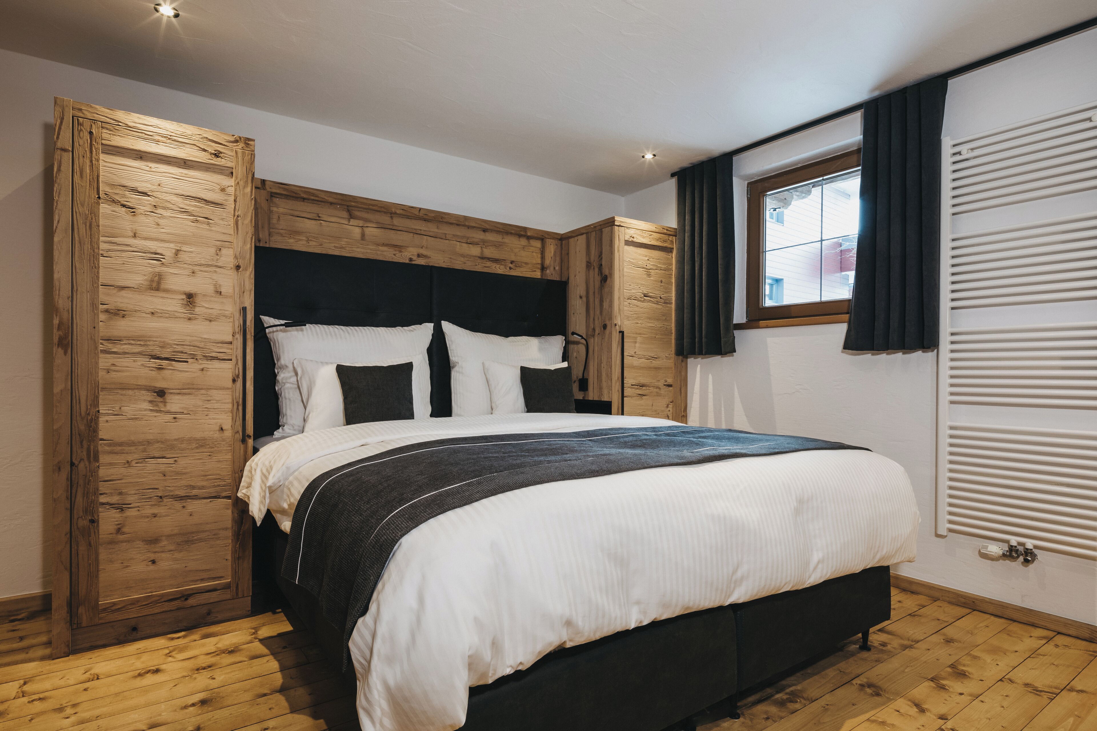 A bedroom with a wooden headboard, a large bed with white bedding, and a window with curtains.