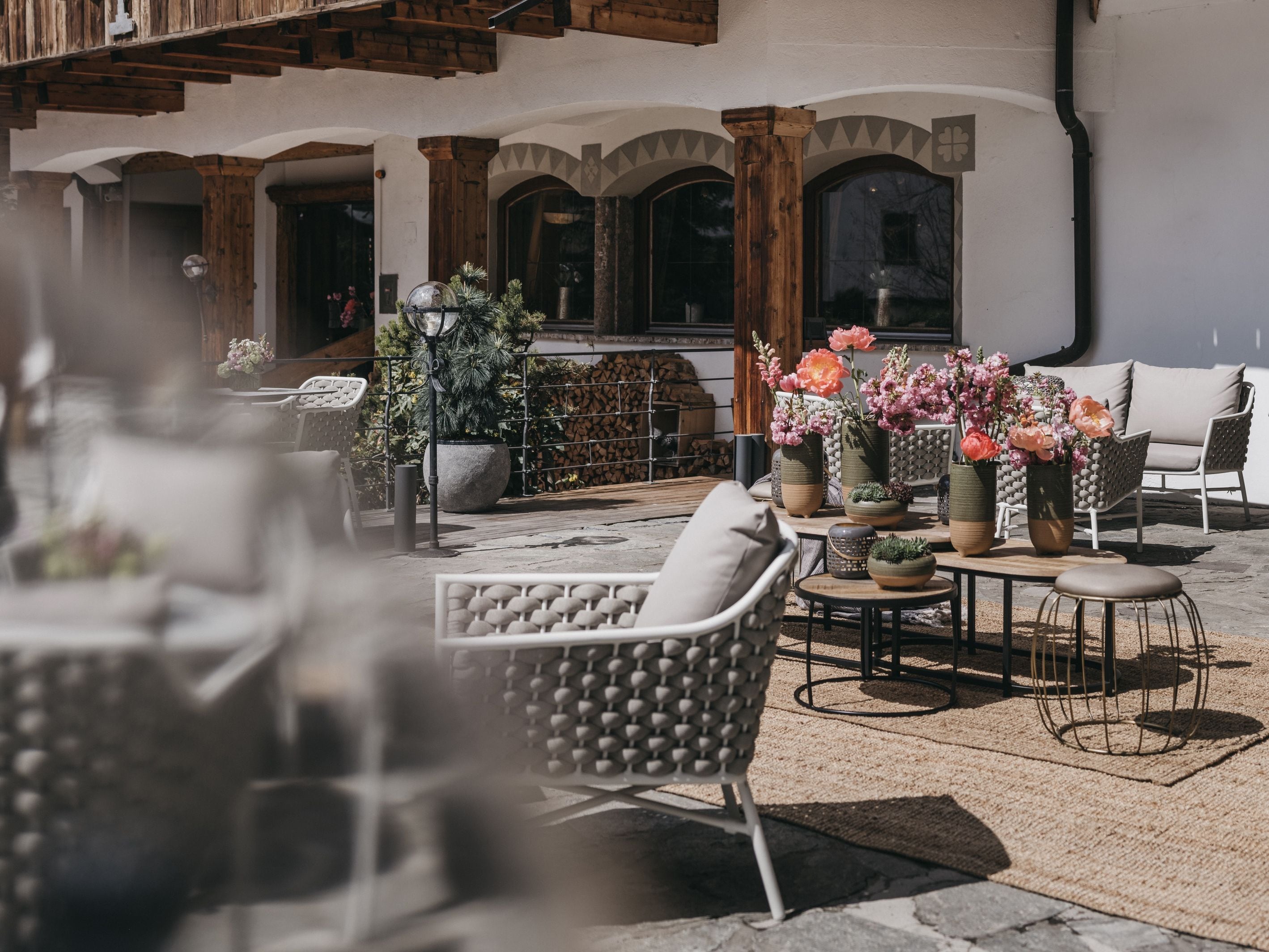 Een terras met rieten stoelen en tafels, potplanten en een stenen vloer.