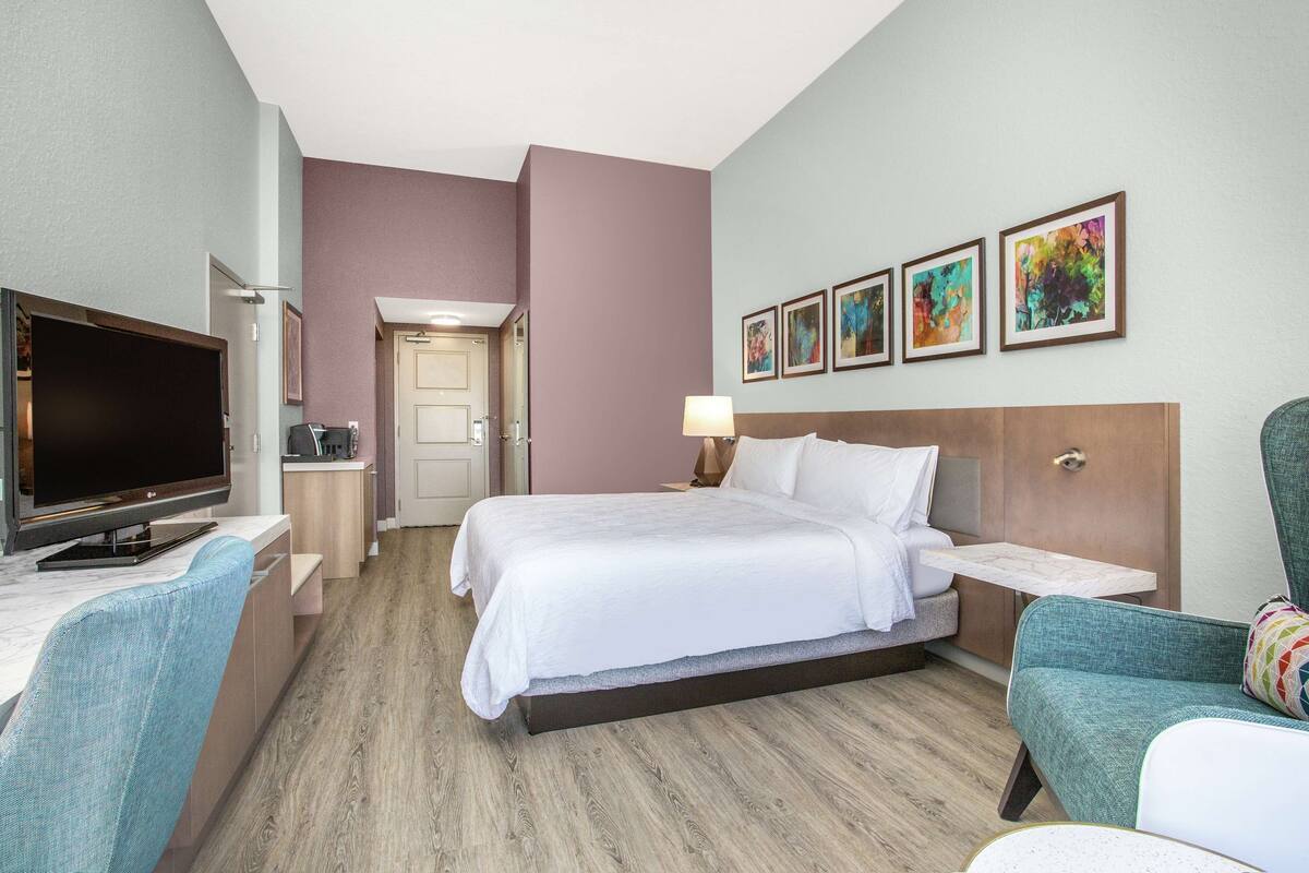 A hotel room with a bed, a TV, a desk, and a chair.