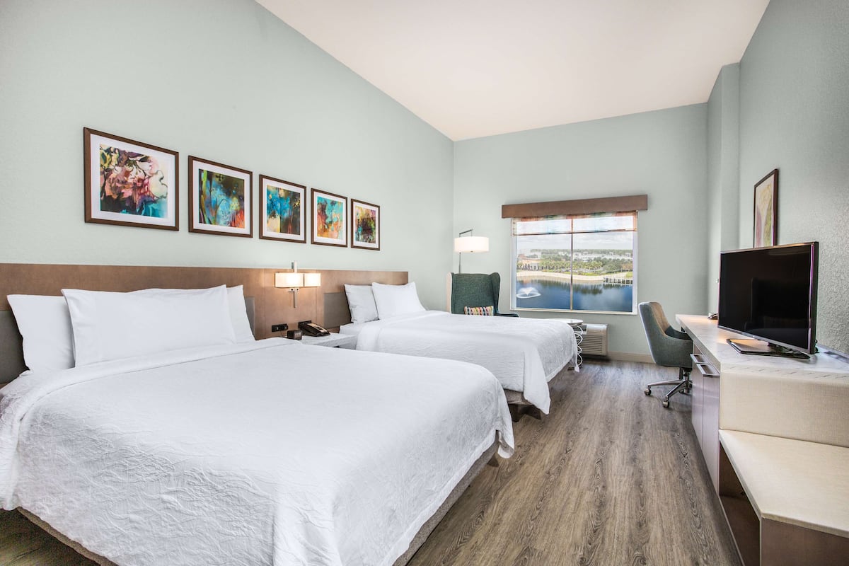 A hotel room with two beds, a desk, a TV, and a window with a view.