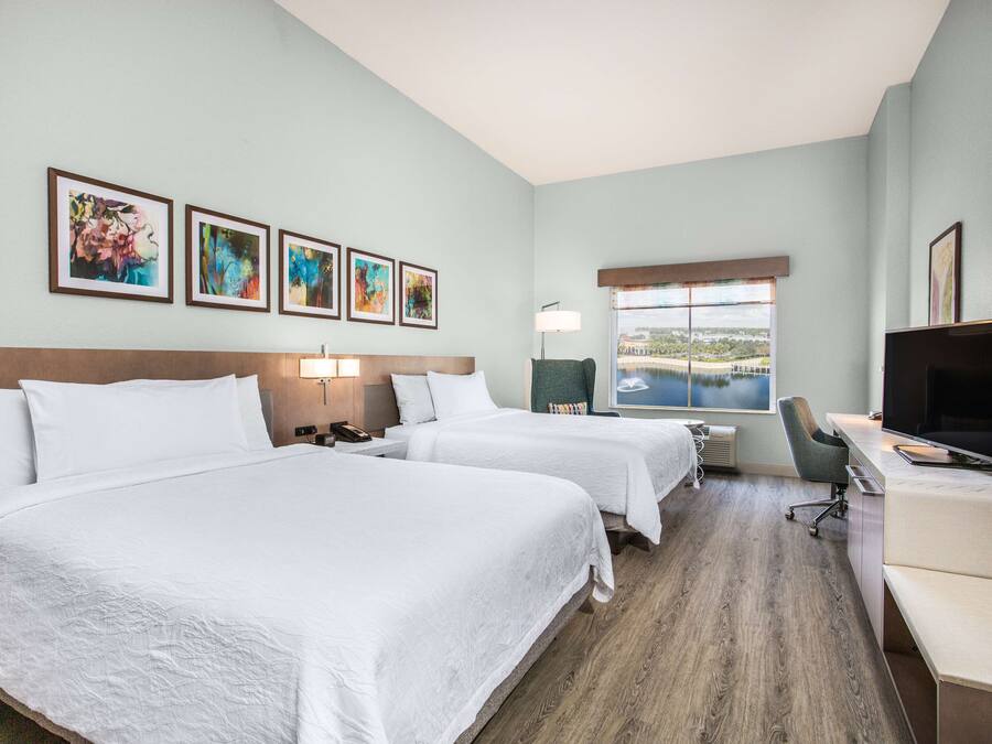 A hotel room with two beds, a desk, a TV, and a window with a view.