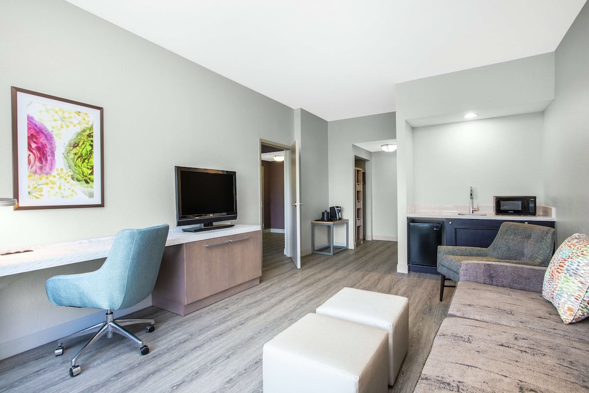 A modern living room with a desk, a television, a sofa, and a kitchen area.