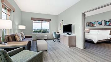 A hotel room with a bed, a desk with a computer, a chair, a sofa, and a window with a view.