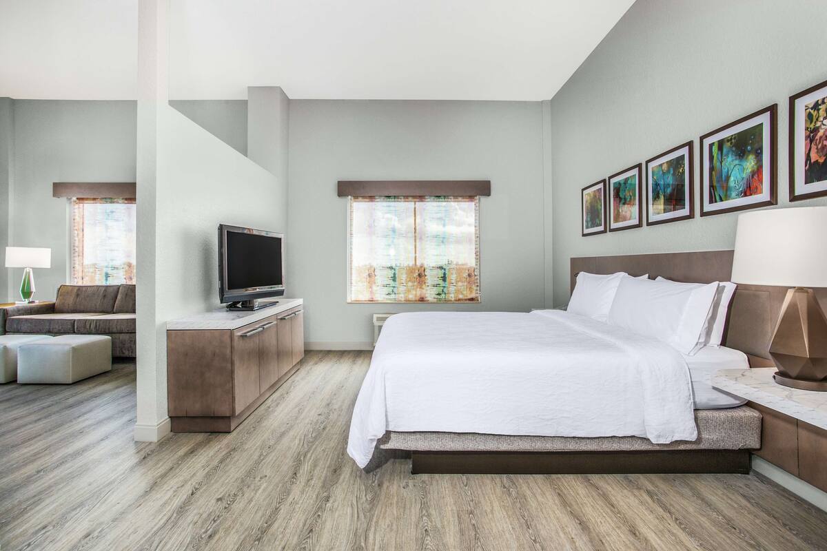 A modern hotel room with a large bed, a flat-screen TV, a sofa, and a desk.