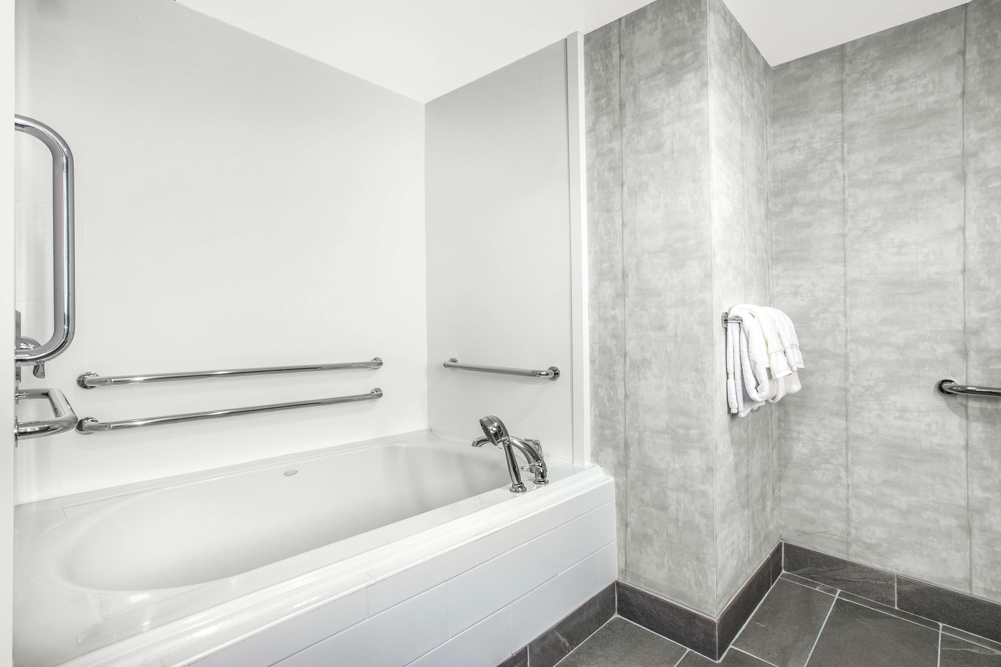 A modern bathroom with a white bathtub, grab bars, and a shower area.