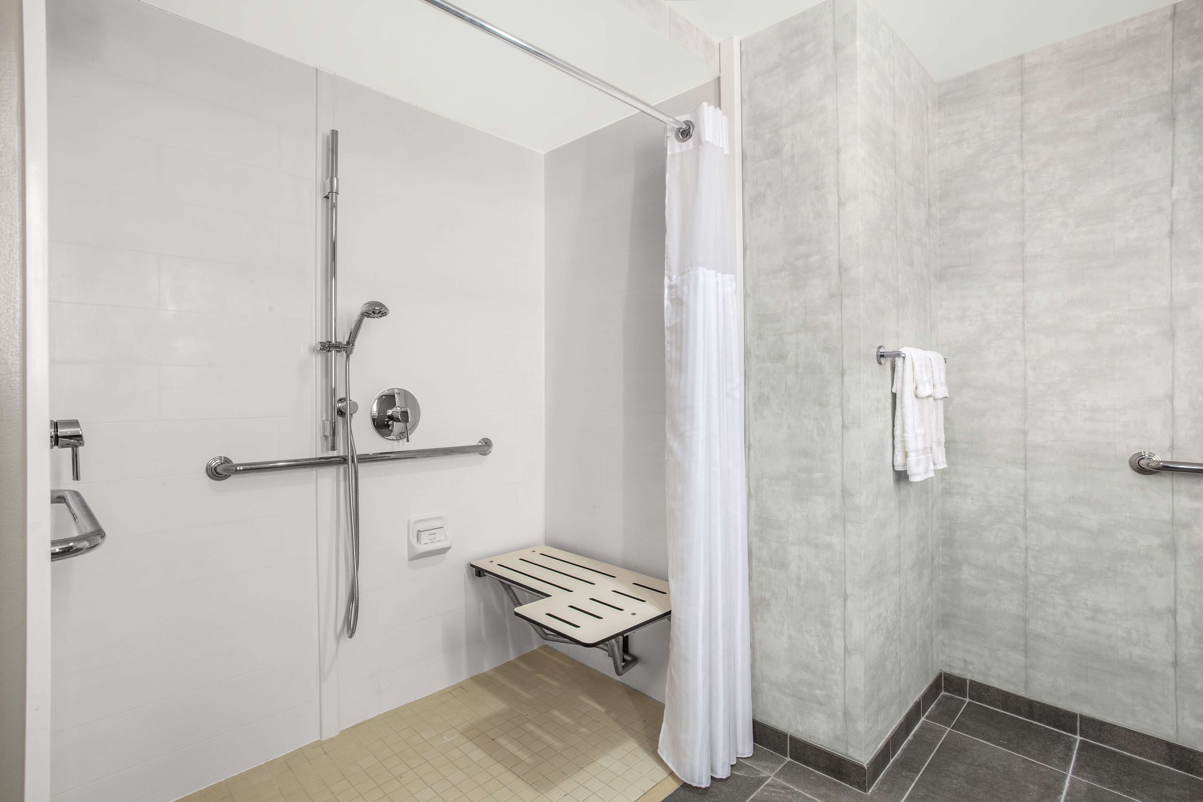 Un baño moderno con ducha, barras de apoyo y un asiento.