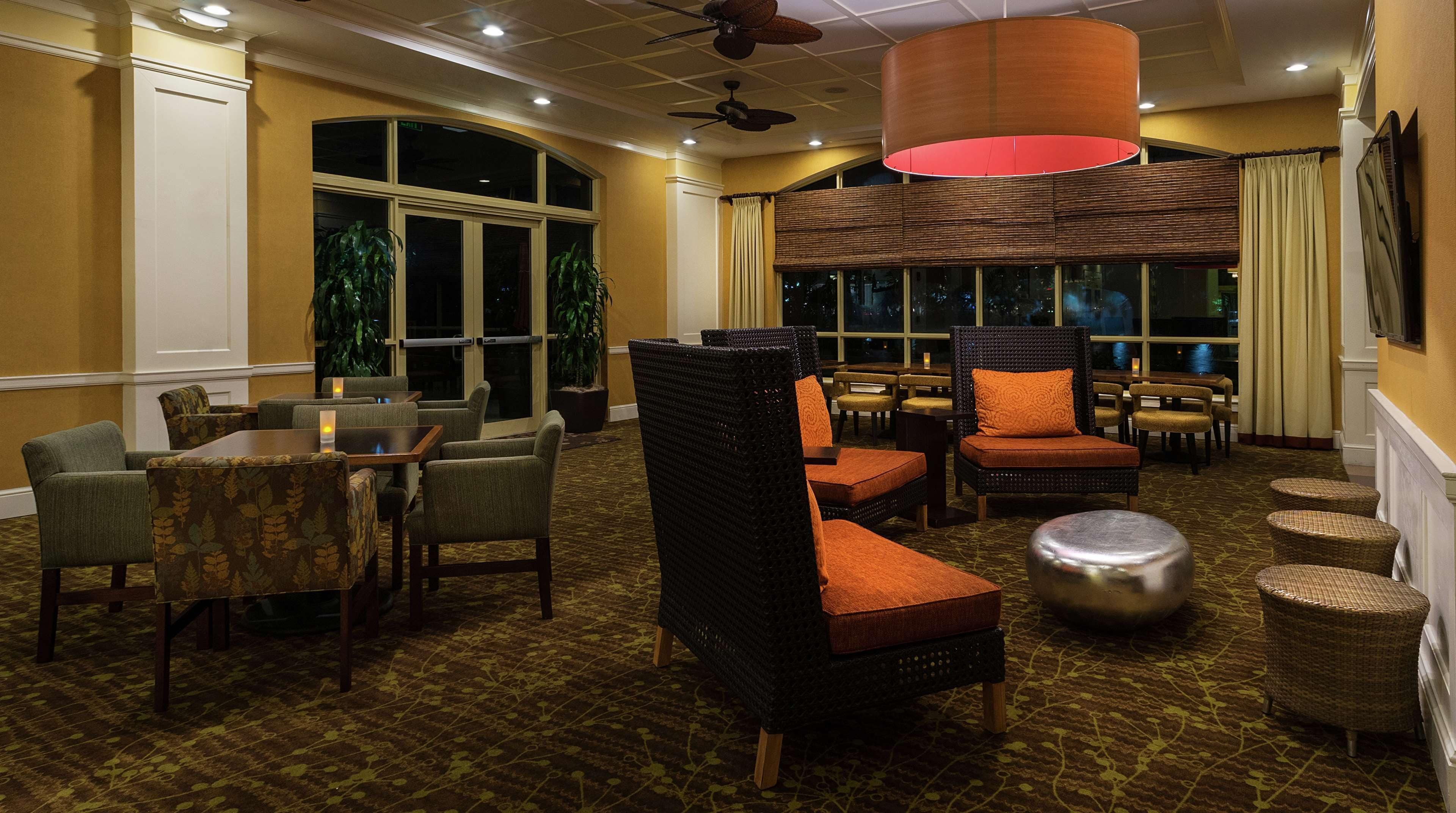 A hotel lobby with a seating area featuring wicker chairs and tables, large windows, and a ceiling fan.