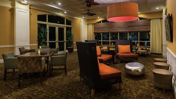 A hotel lobby with a seating area featuring wicker chairs and tables, large windows, and a ceiling fan.