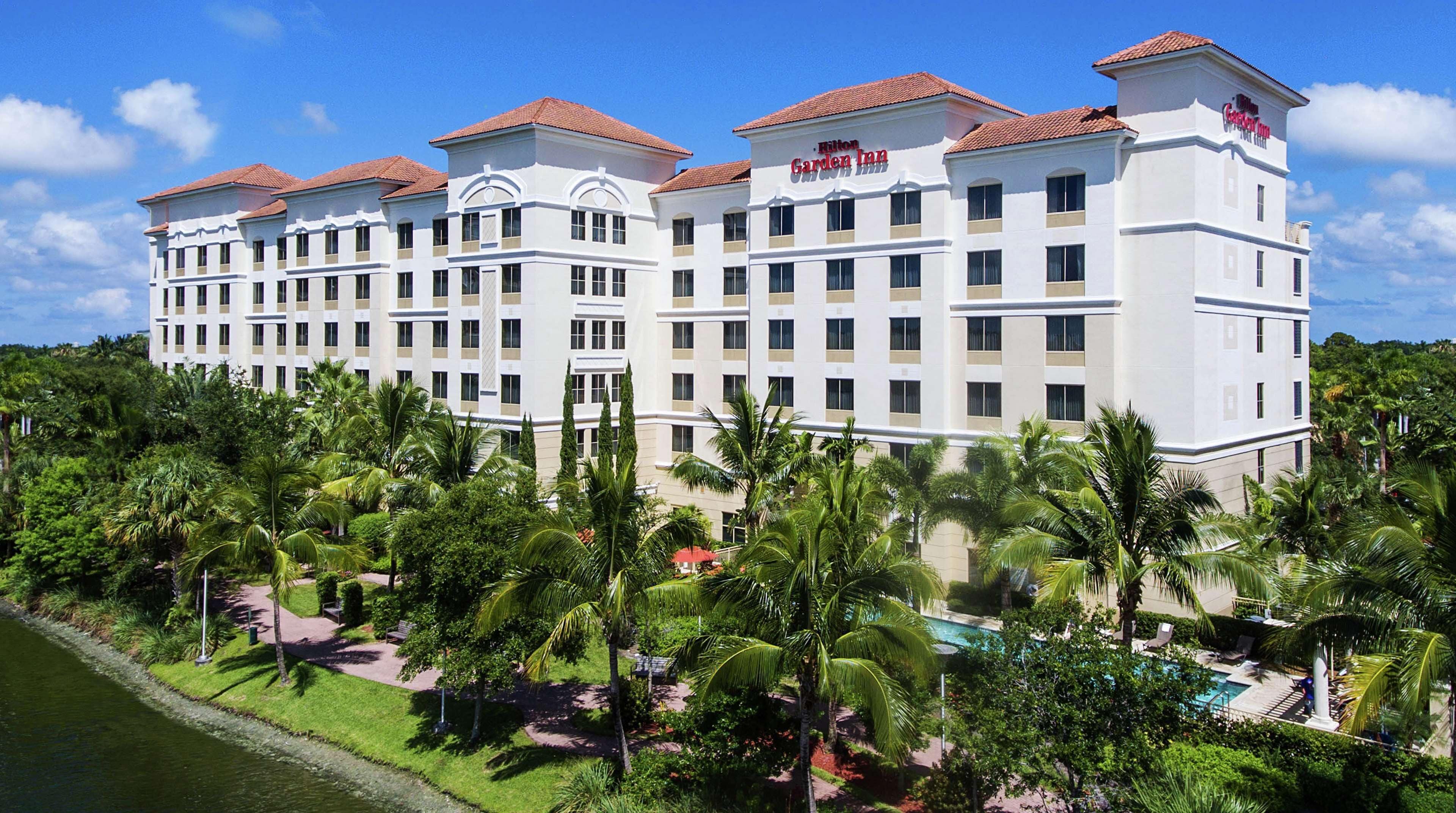 A large, multi-story hotel with a white facade and red-tiled roofs, surrounded by lush greenery and a pool area.