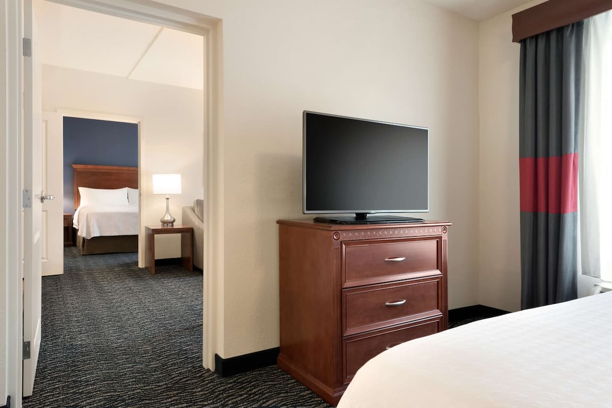 A hotel room with a bed, a TV on a wooden dresser, a nightstand, and a lamp.