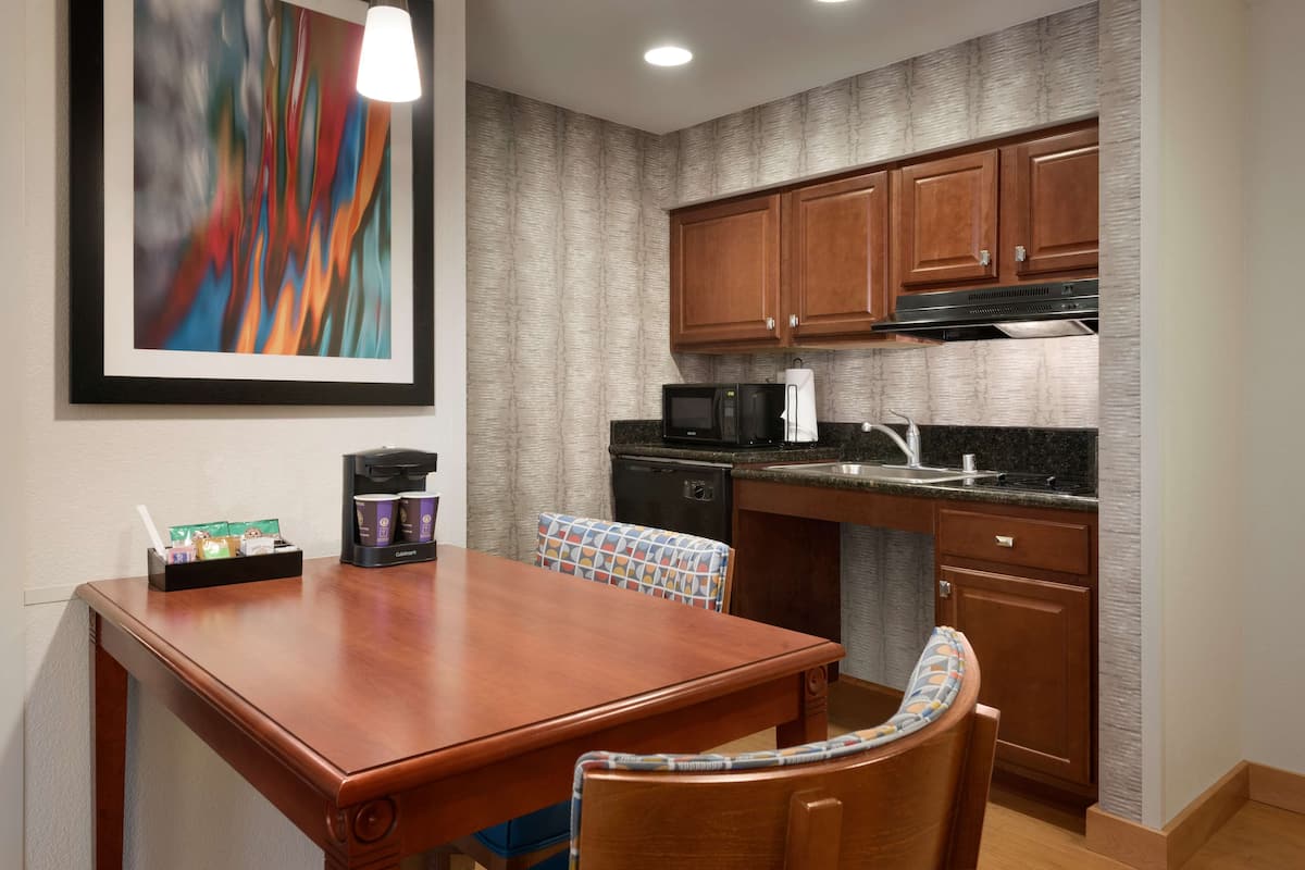 A kitchen with wooden cabinets, a microwave, a coffee maker, and a dining table with chairs.