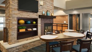 A modern dining area with a stone fireplace, a flat-screen TV mounted above, and a seating arrangement with a round table and chairs.