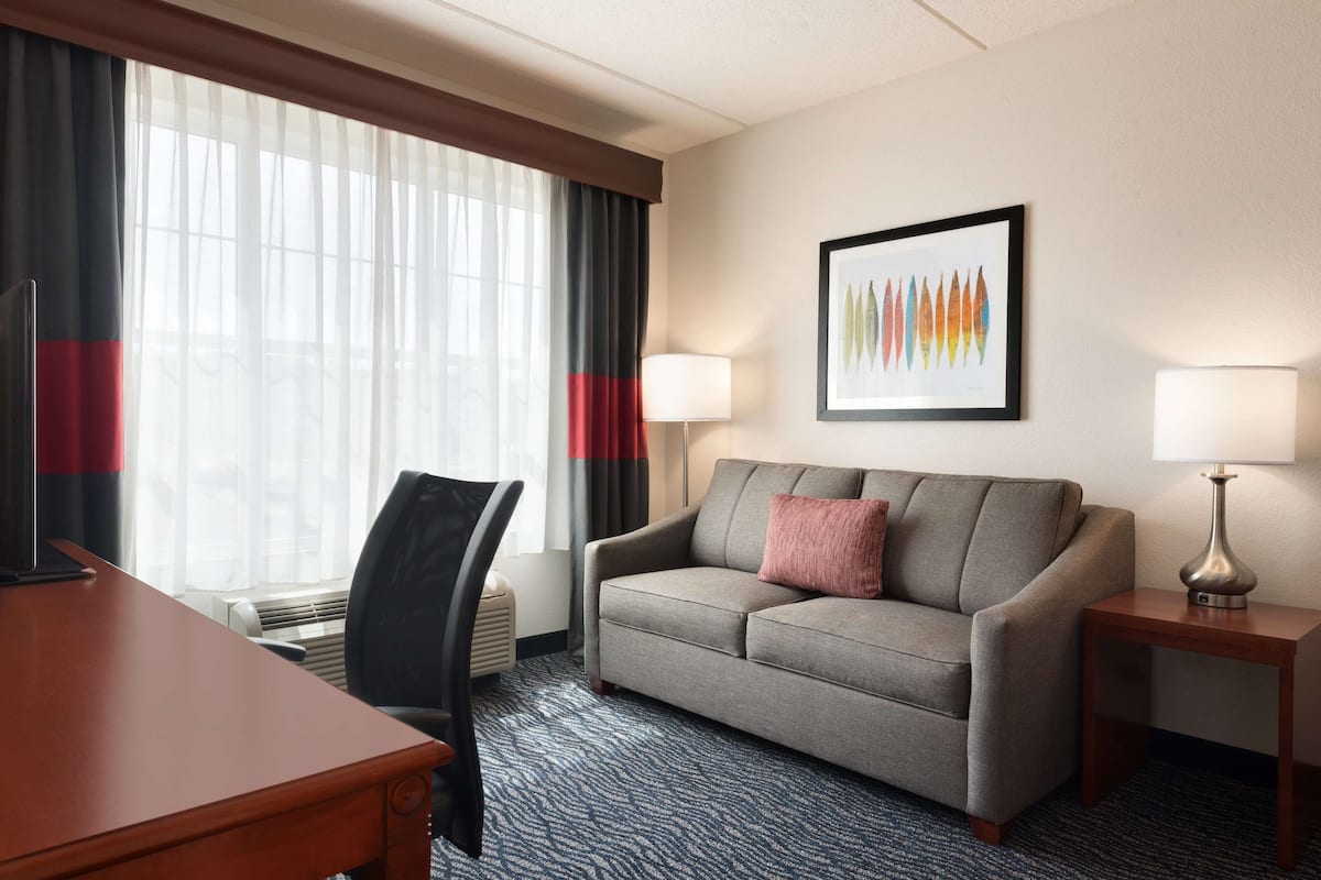 A hotel room with a sofa, a desk, a chair, two lamps, and a framed picture on the wall.