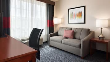 Habitación de hotel con sofá, escritorio, una silla, dos lámparas y un cuadro en la pared.