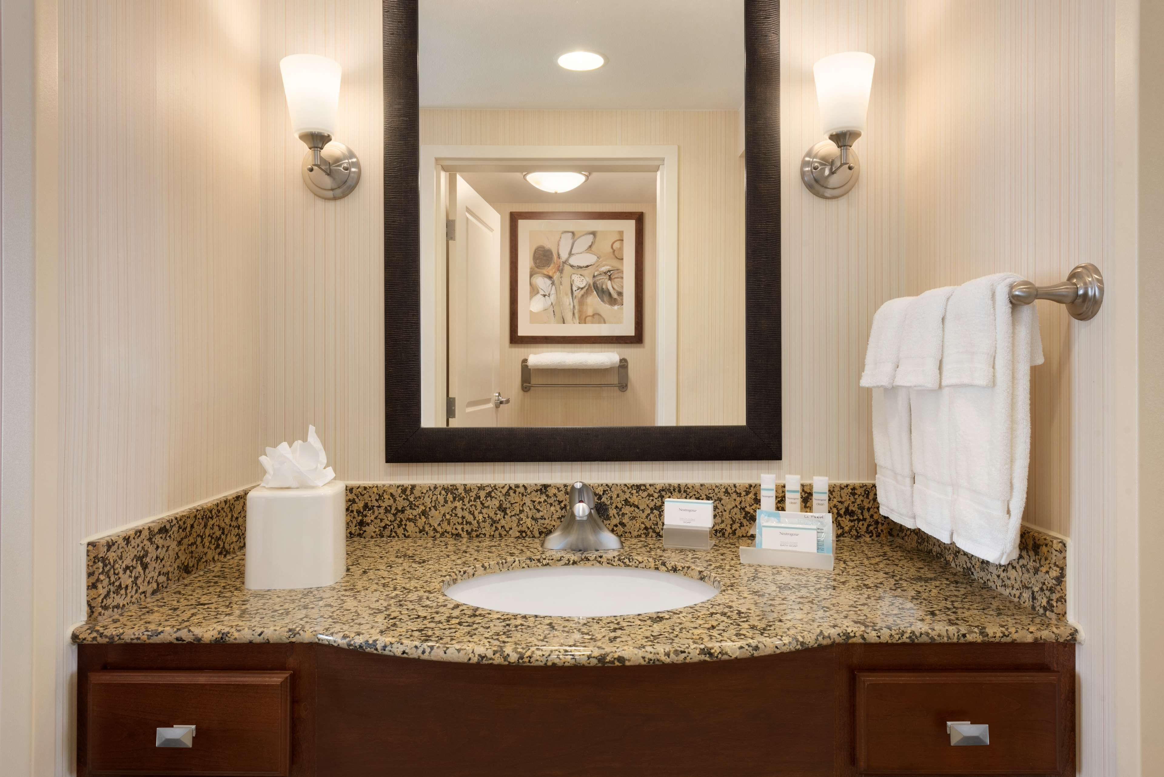 A bathroom with a granite countertop, a sink, a mirror, and a towel rack.