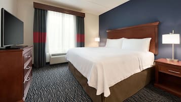 A hotel room with a large bed, a flat-screen TV, a desk with a lamp, and a window with curtains.