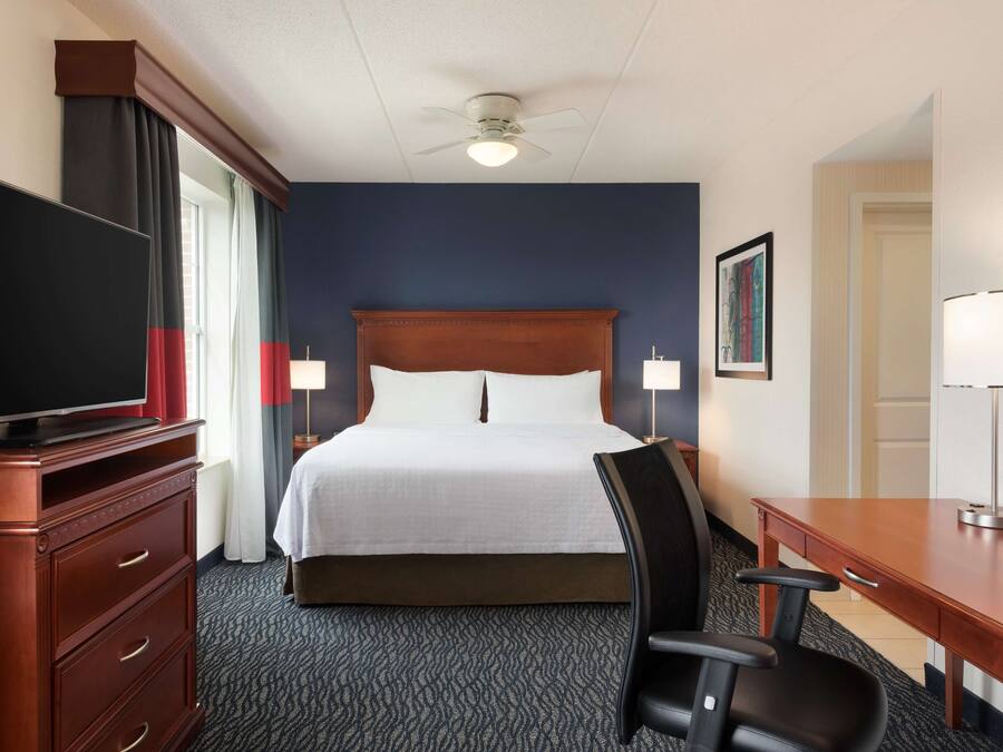 Hotelkamer met een groot bed, een televisie op een houten dressoir, een bureau met stoel en een plafondventilator.