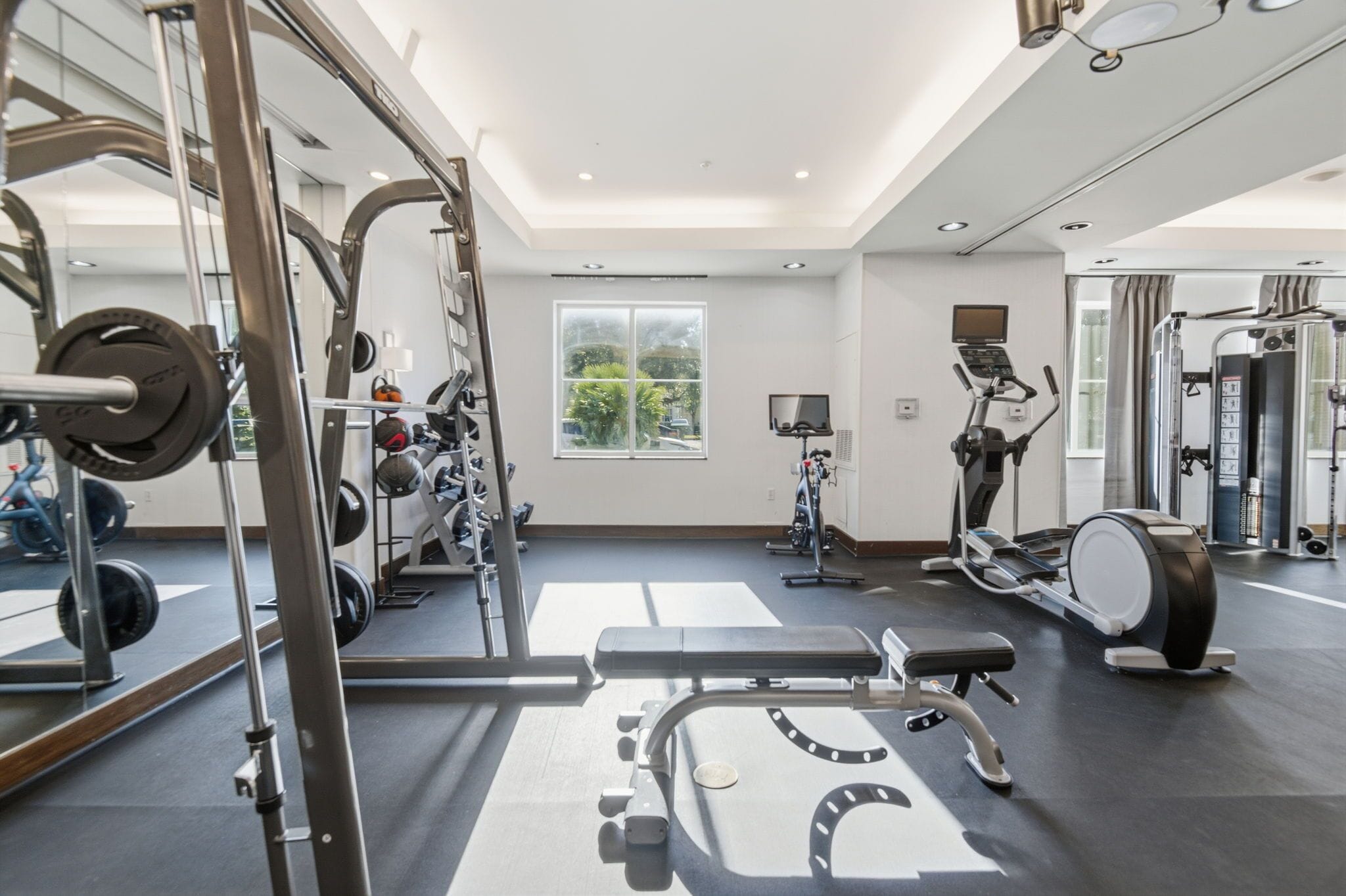 A gym with exercise equipment, a large mirror, and a window with a view of greenery.