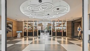 Un vestíbulo de hotel con piso a cuadros, un felpudo negro que dice "KOMPOS HOTEL" y una lámpara de araña moderna.