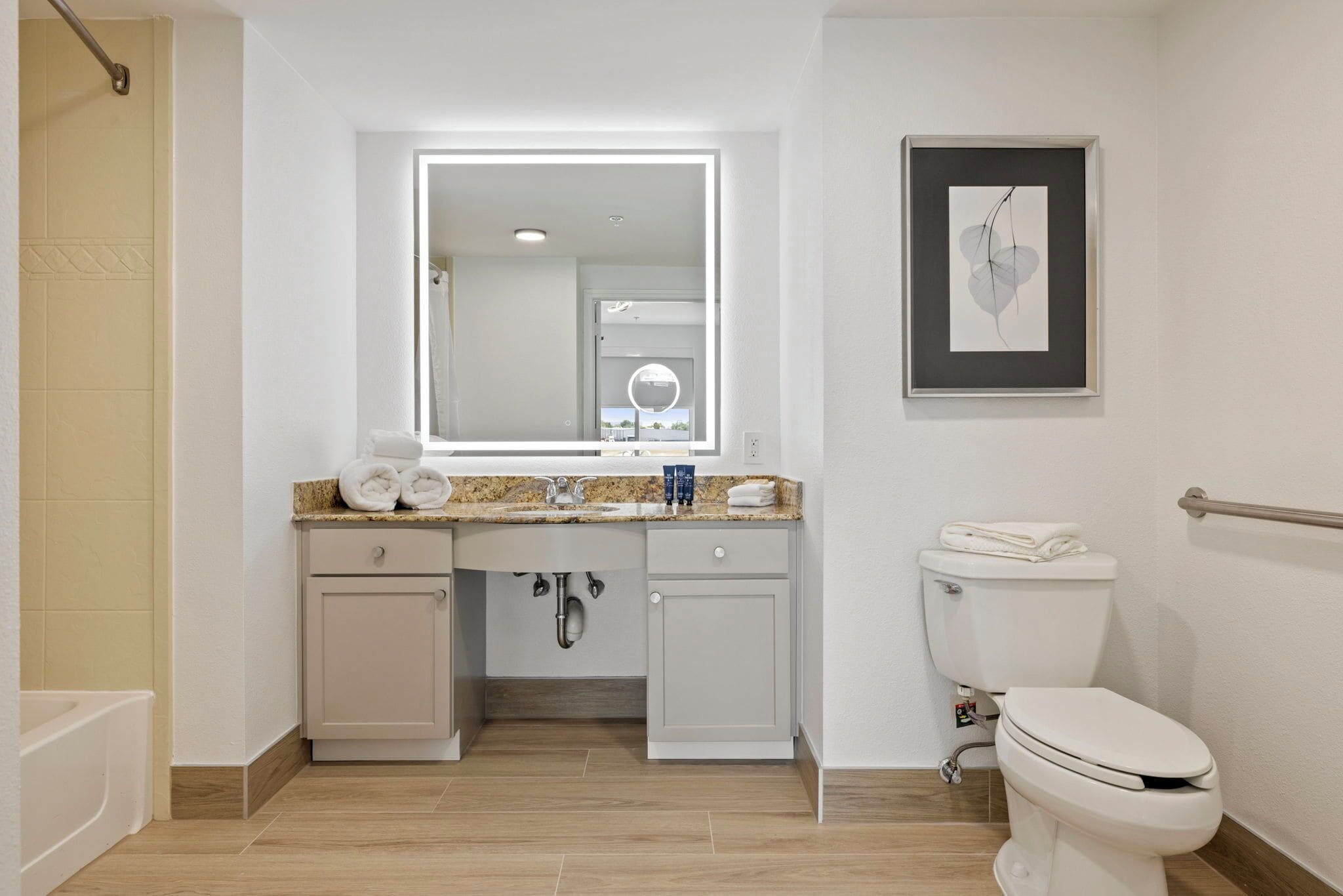 A modern bathroom with a vanity, sink, mirror, toilet, and a framed artwork on the wall.