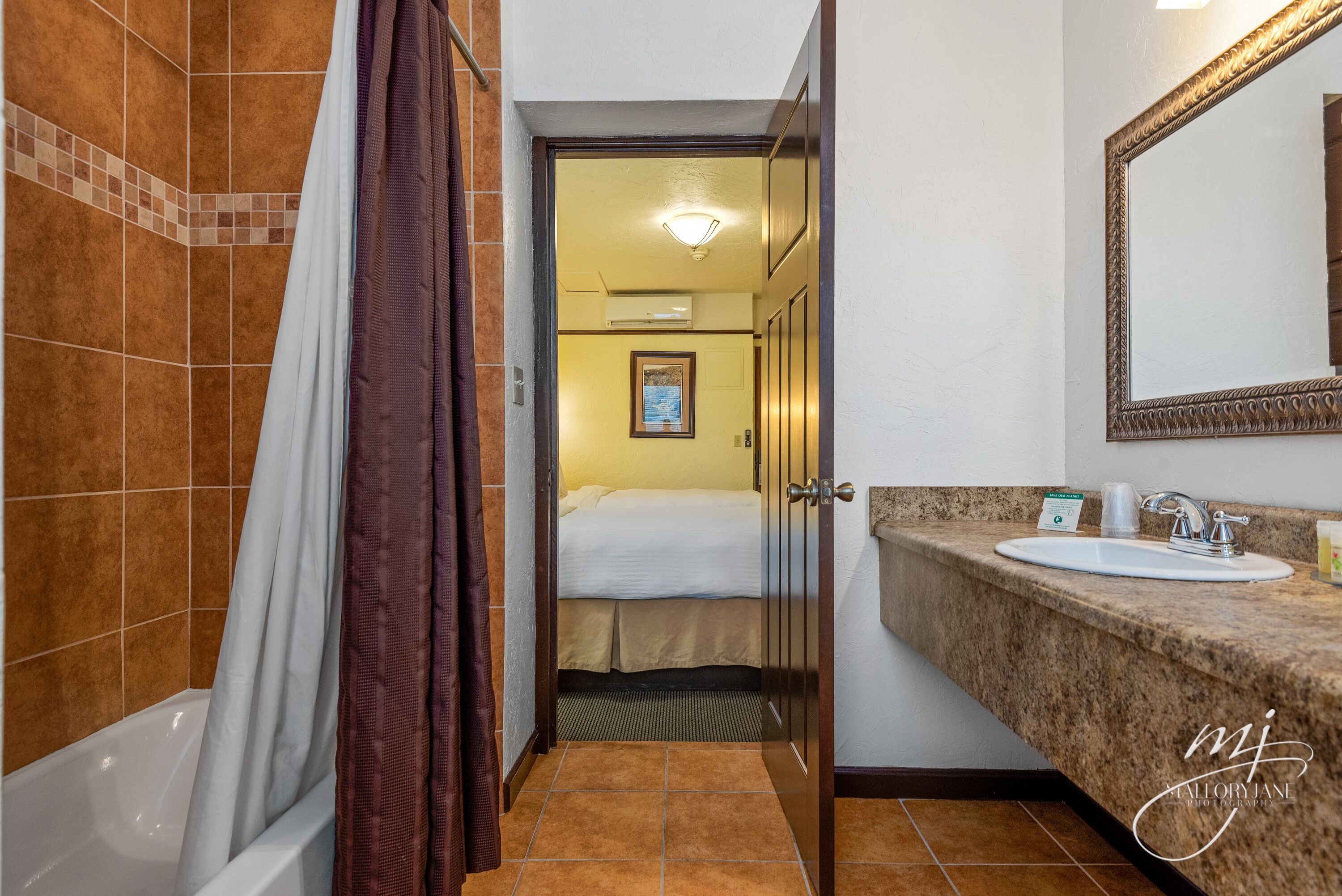 A hotel bathroom with a bathtub, shower curtain, sink, and mirror.