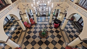 A lobby with a checkered floor, red seating, a chandelier, and decorative wall patterns. - Hotel Seville (Harrison)