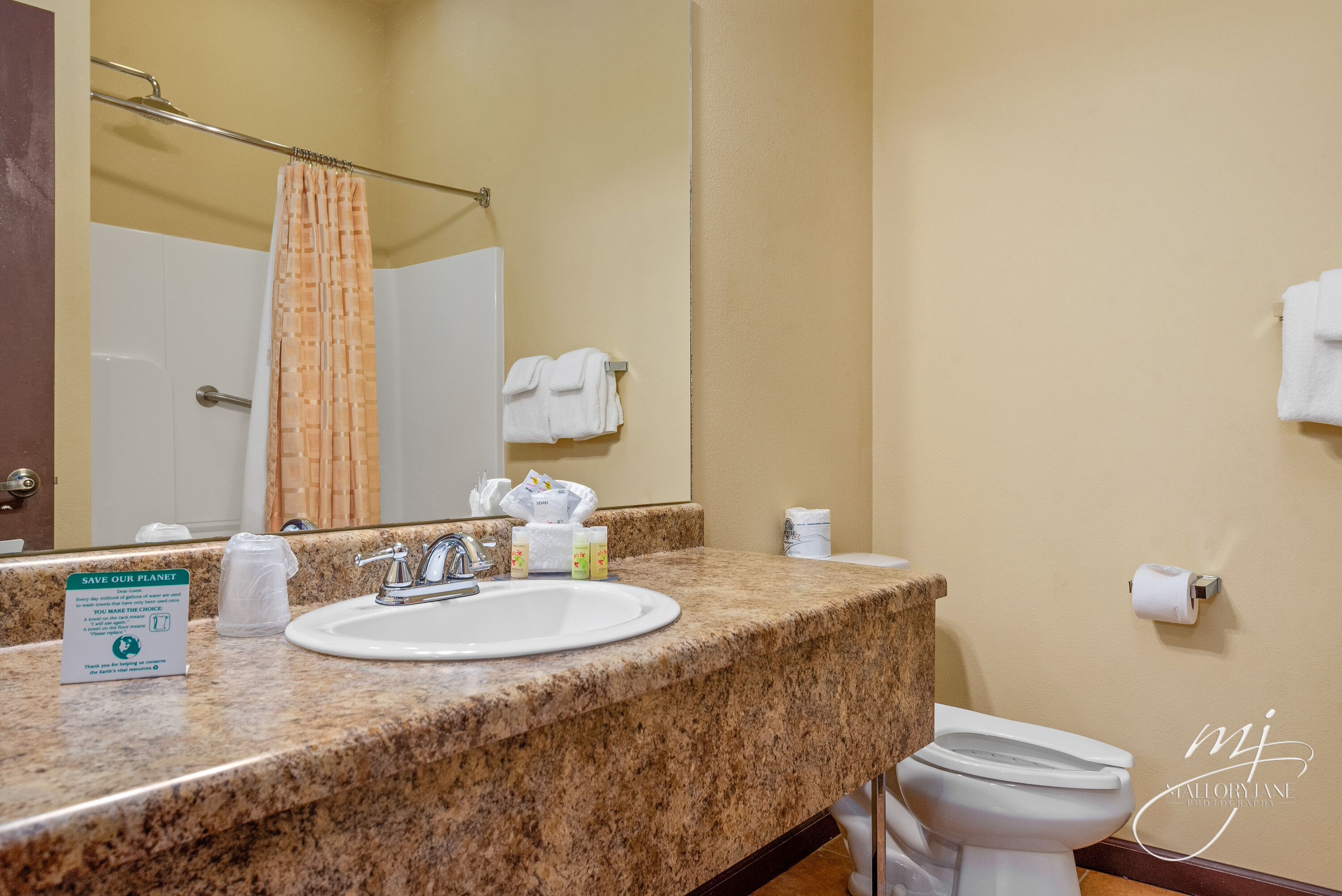 A hotel bathroom with a granite countertop, a white sink, a mirror, a shower curtain, and a toilet.