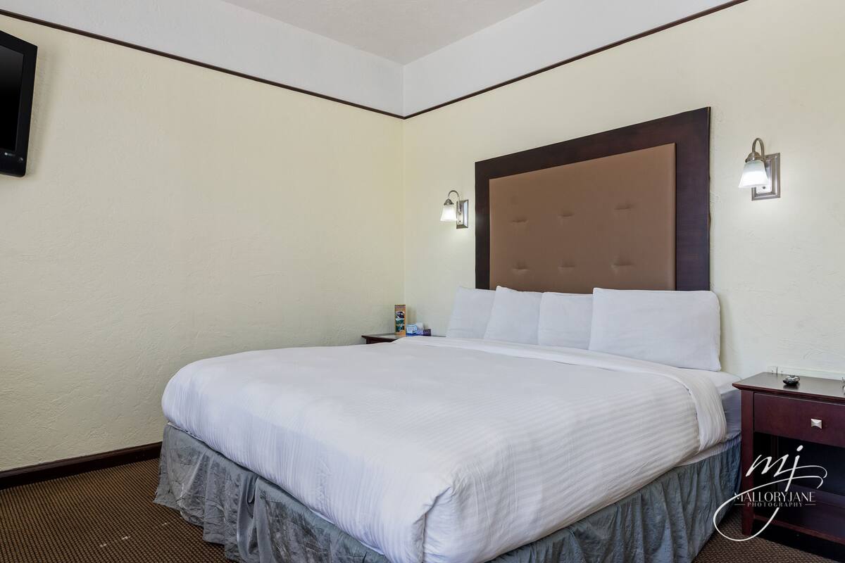 A neatly made bed with a large headboard, two bedside tables with lamps, and a wall-mounted TV.