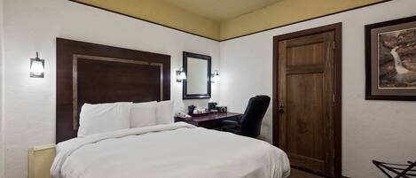 Een hotelkamer met een groot bed, een bureau met stoel, een houten deur en een lijst met een afbeelding aan de muur.