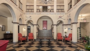 A lobby with a checkered floor, red chairs, a central table, and a staircase leading to an upper level. - Hotel Seville (Harrison)