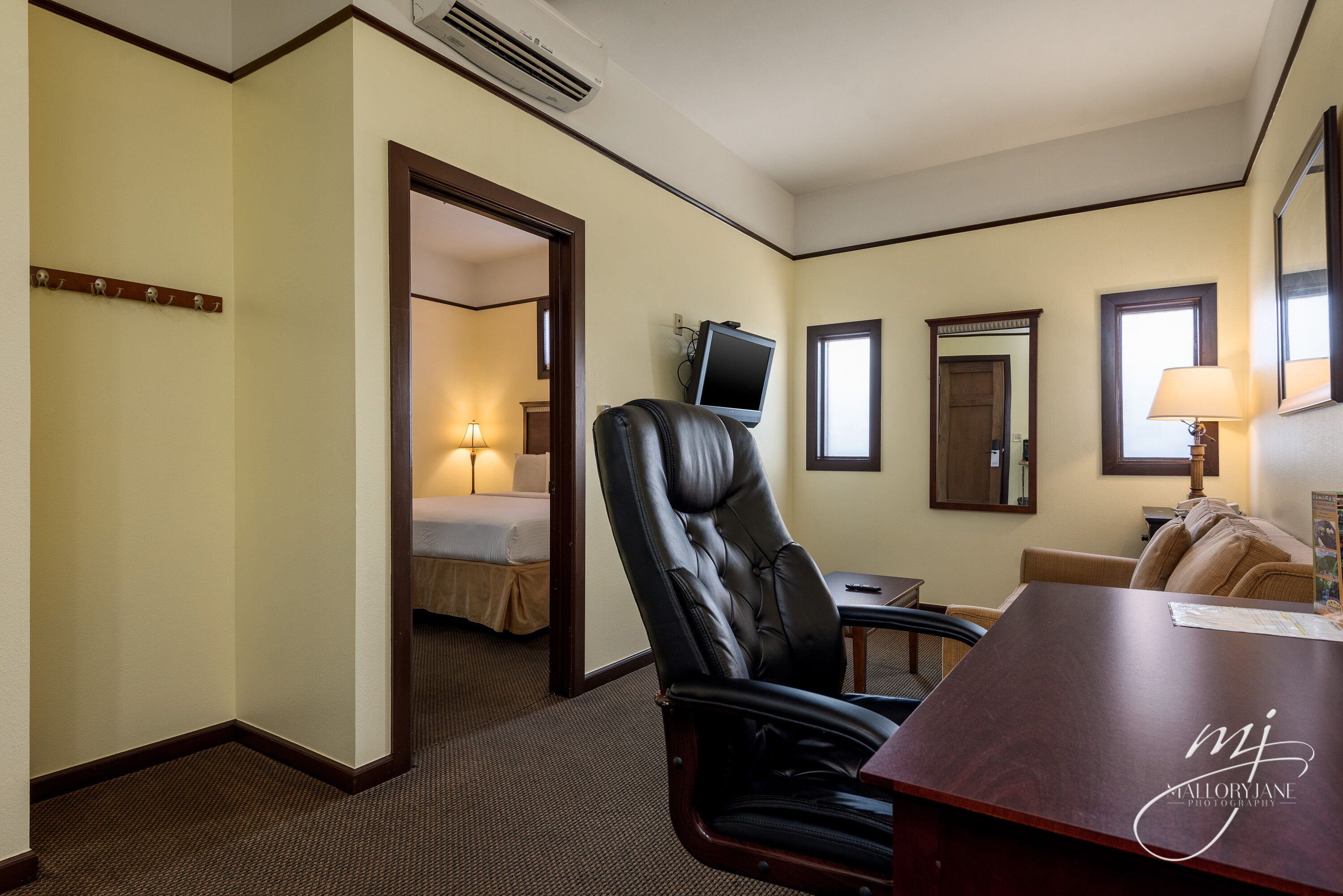 Ein Hotelzimmer mit großem Ledersessel, Schreibtisch, Bett und Fernseher.