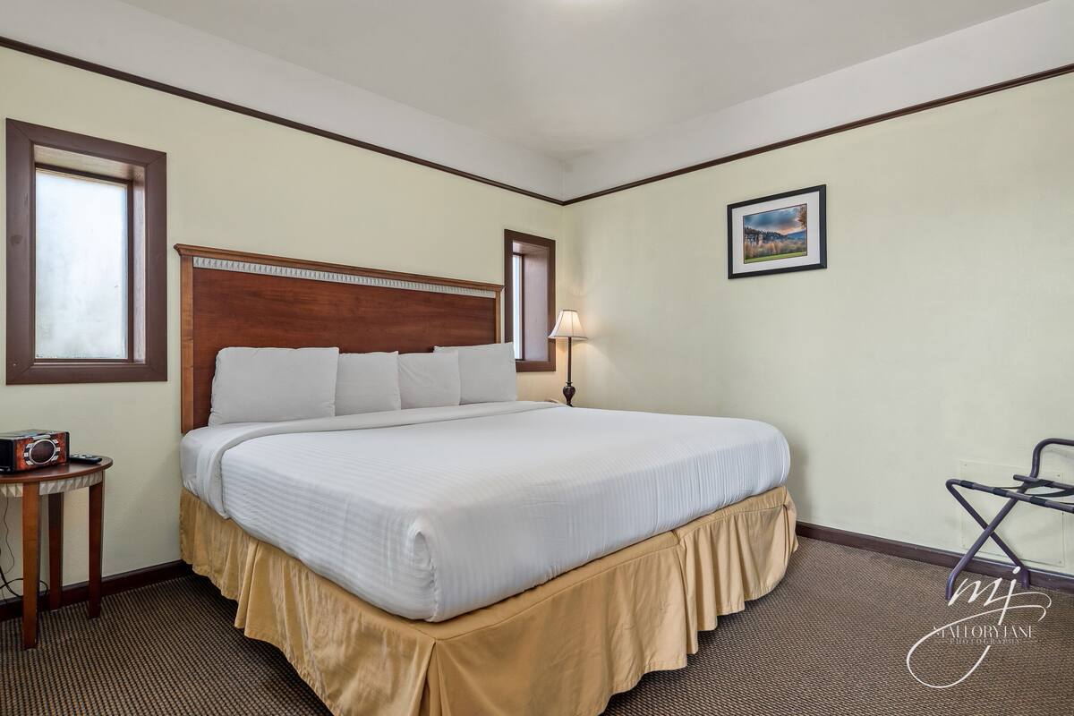 A neatly made bed with a wooden headboard, a bedside table with a radio, and a picture on the wall.