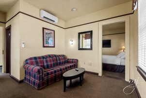 Habitación de hotel con sofá de cuadros, una mesita, una cama, televisión y aire acondicionado.