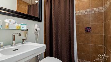 Une salle de bain avec un lavabo blanc, un miroir, un distributeur de serviettes et un rideau de douche.