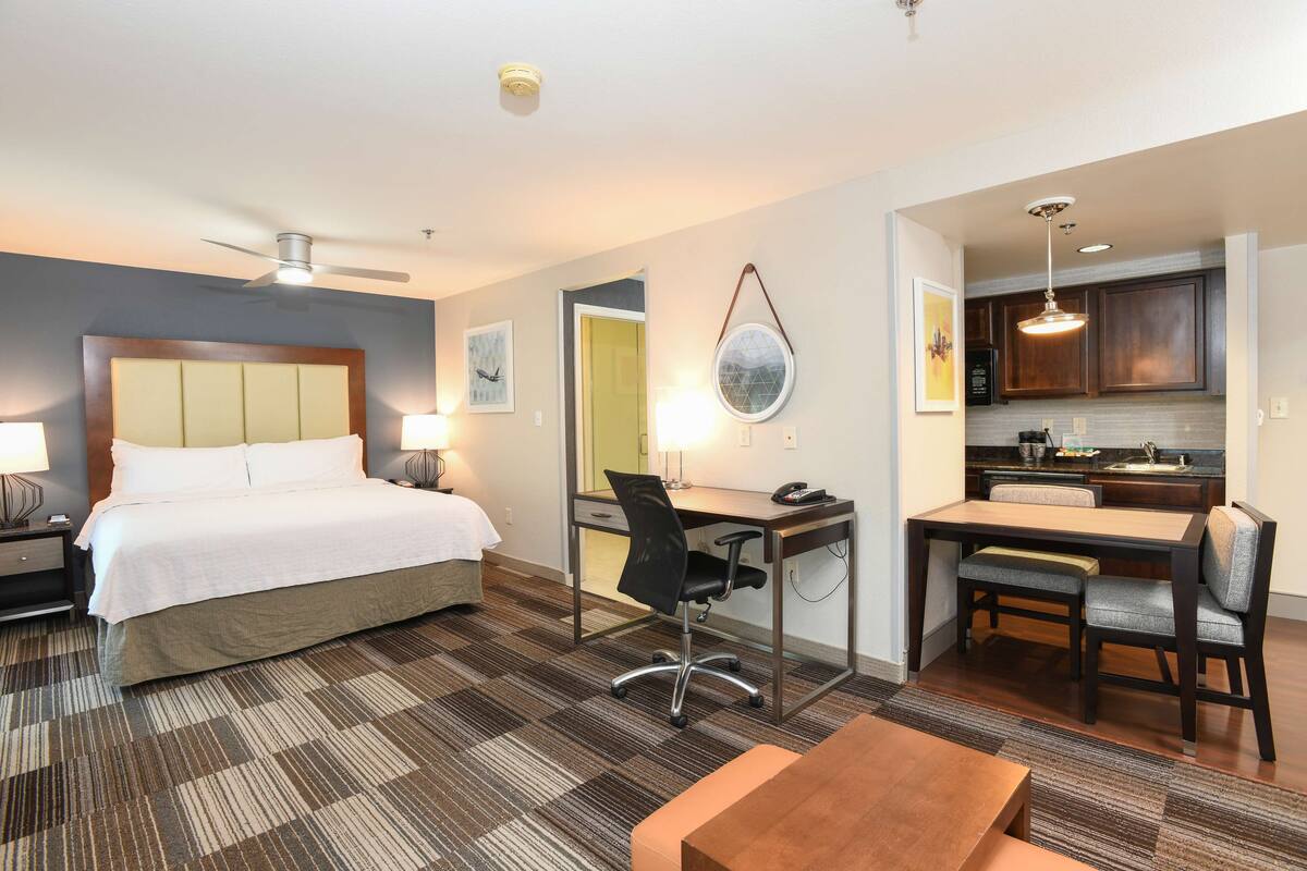 A hotel room with a bed, desk, chair, and kitchenette.