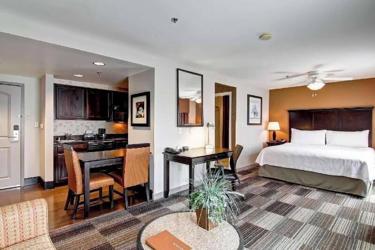 A hotel room with a bed, a desk, a chair, a dining table, and a kitchen area.