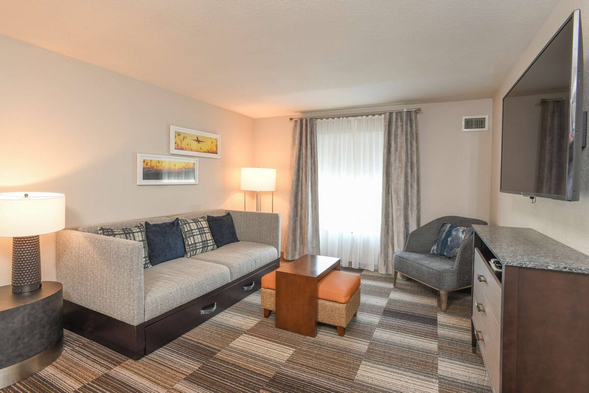 A hotel room with a sofa, a small table, a chair, a desk, and a TV.