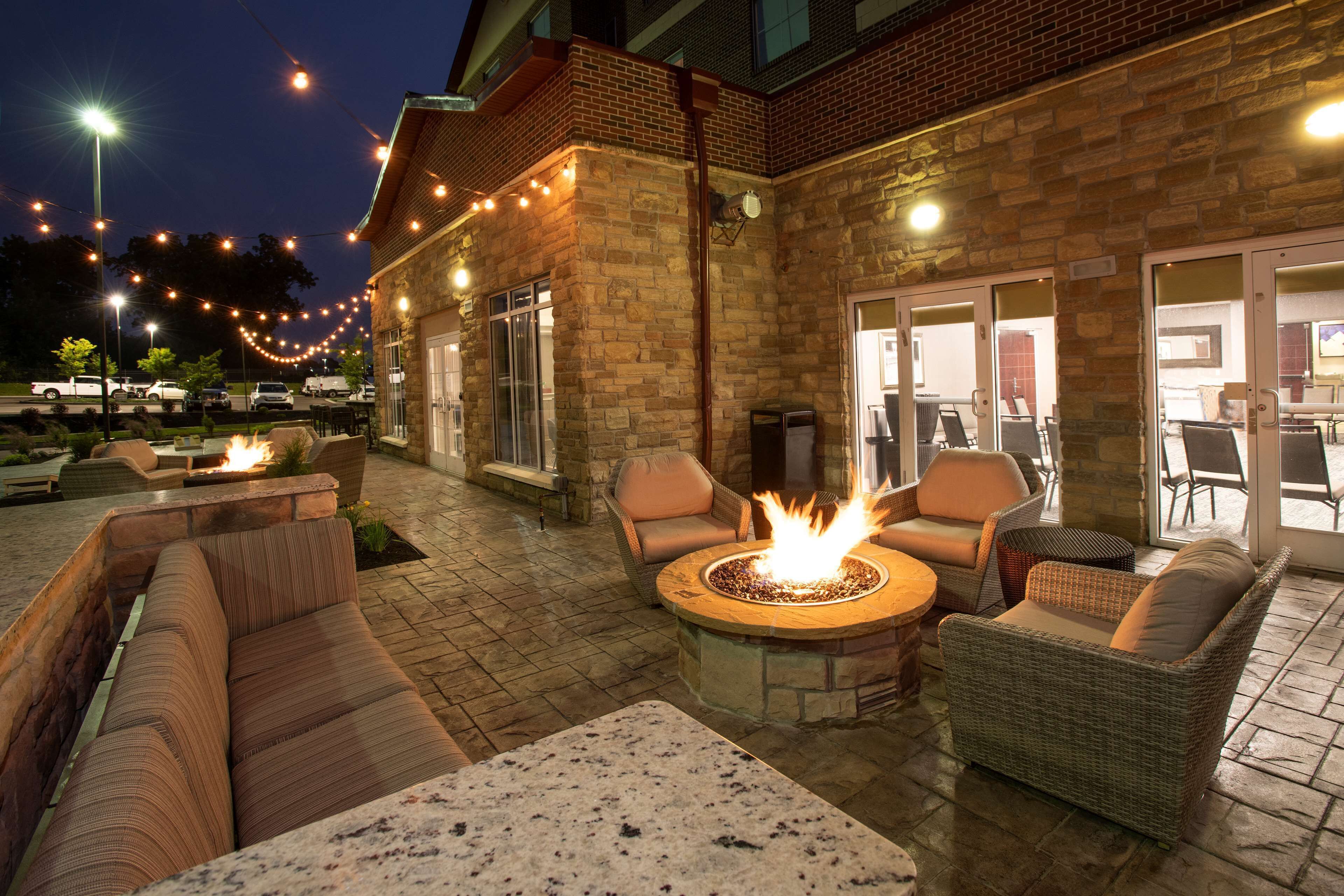 An outdoor patio area with stone walls, wicker furniture, a fire pit, and string lights.