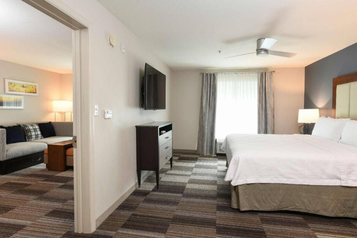 A hotel room with a bed, a desk, a TV, a ceiling fan, and a window with curtains.