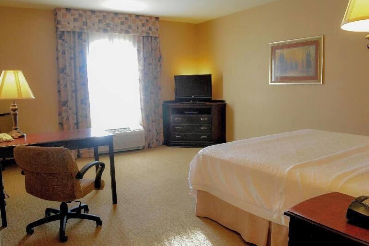 A hotel room with a bed, desk, chair, television, and a painting on the wall.