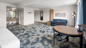 A modern hotel room with a large bed, a round table, a blue sofa, and a wooden bench.