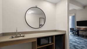 A hotel room with a sink, mirror, microwave, and a television in the corner.